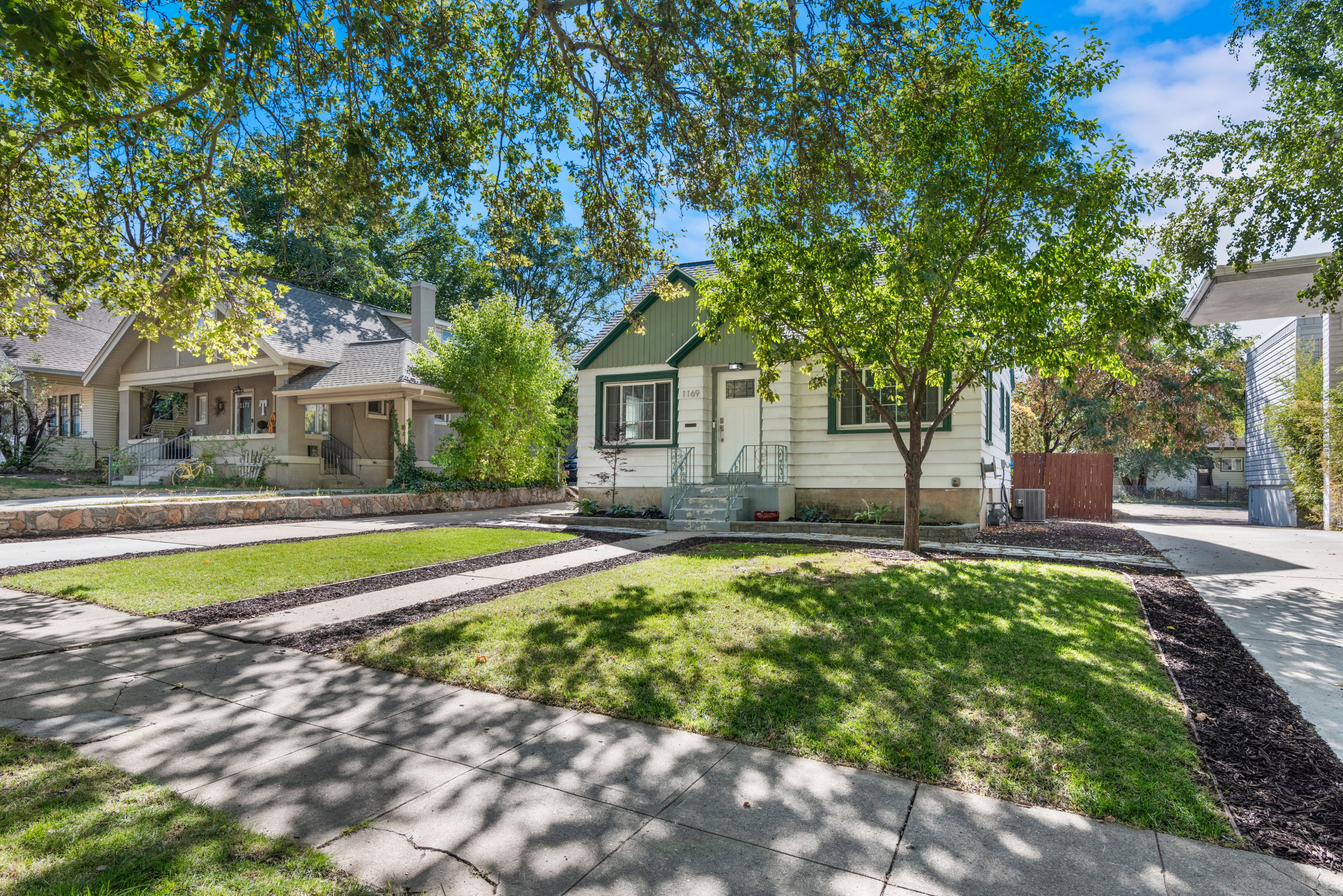 Charming single-family residence featuring a white and green exterior with front porch, well-manicured landscaping, and mature trees