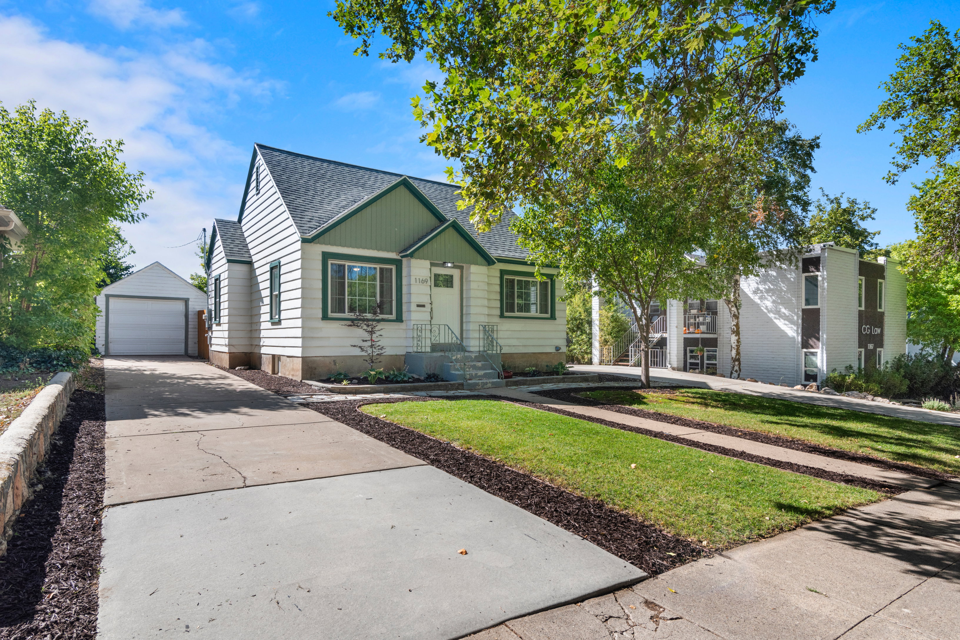 Charming single-family residence featuring a white and green exterior with front porch, well-manicured landscaping, and detached garage