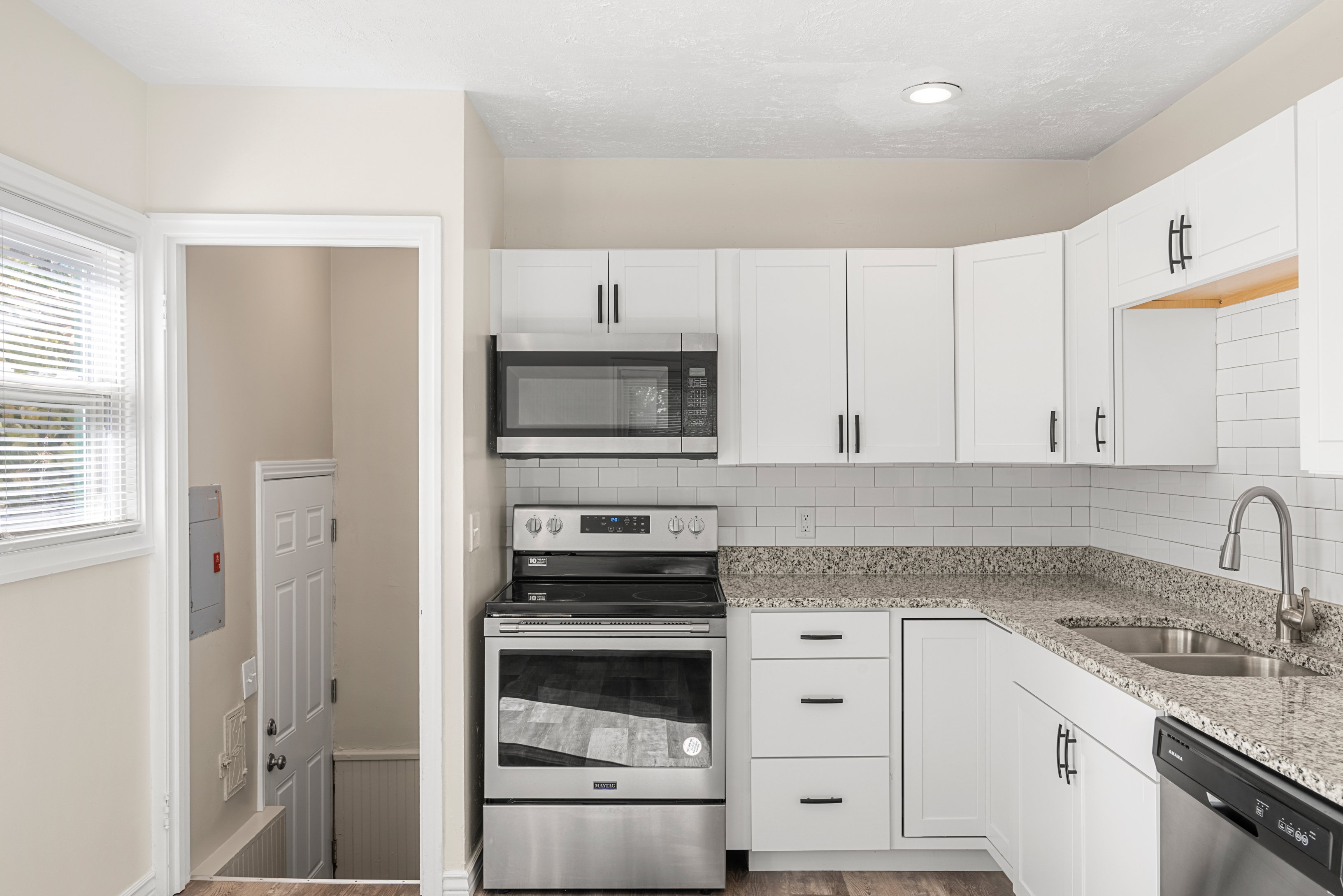 Remodeled kitchen featuring white cabinetry, granite countertops, subway tile backsplash, stainless steel appliances, and recessed lighting