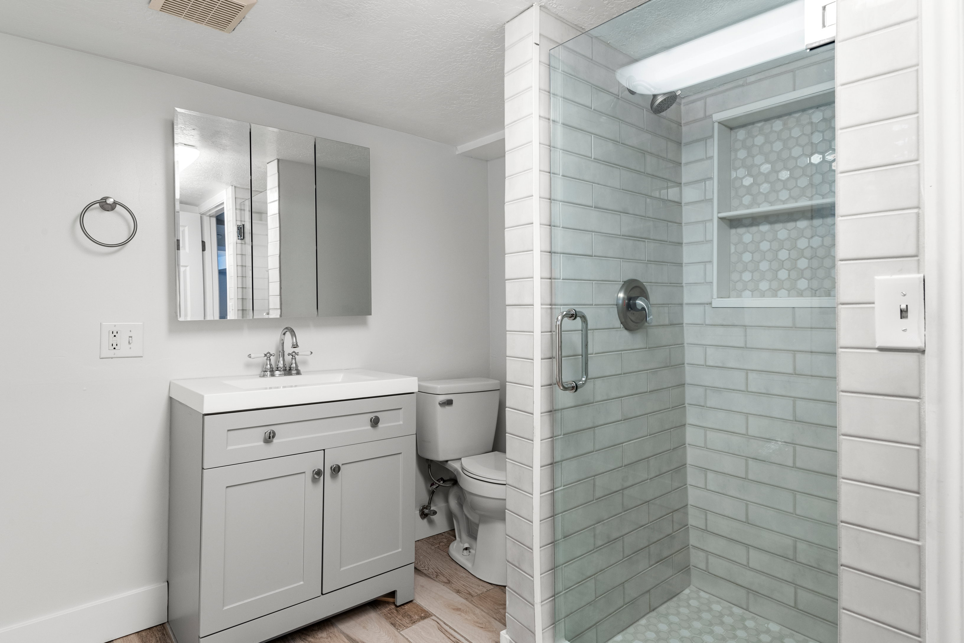 Basement bathroom featuring updated euro-glass shower with custom tile and niche, neutral painted vanity, and laundry space