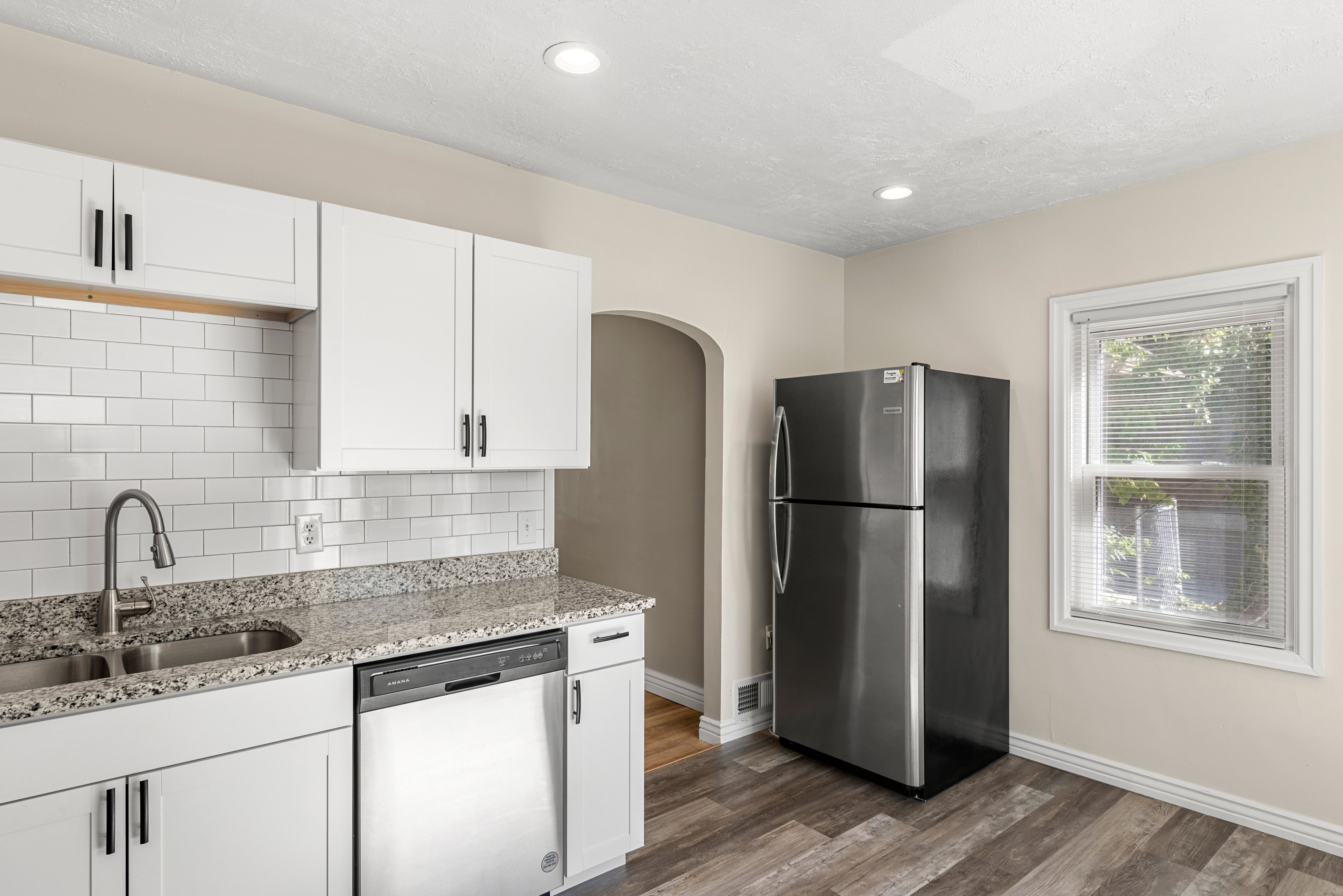 Remodeled kitchen featuring white cabinetry, granite countertops, subway tile backsplash, stainless steel appliances, and recessed lighting
