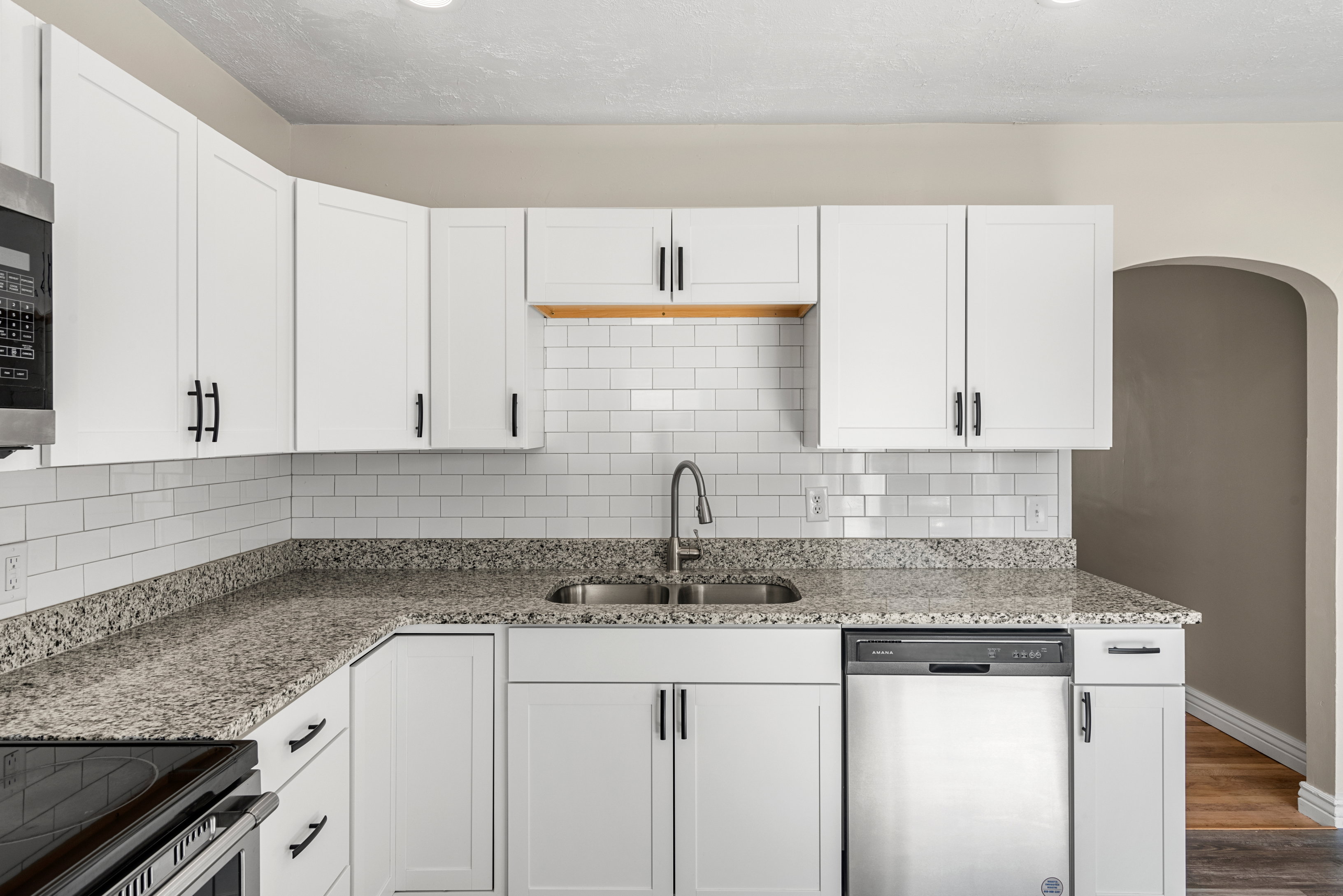 Remodeled kitchen featuring white cabinetry, granite countertops, subway tile backsplash, stainless steel appliances, and recessed lighting