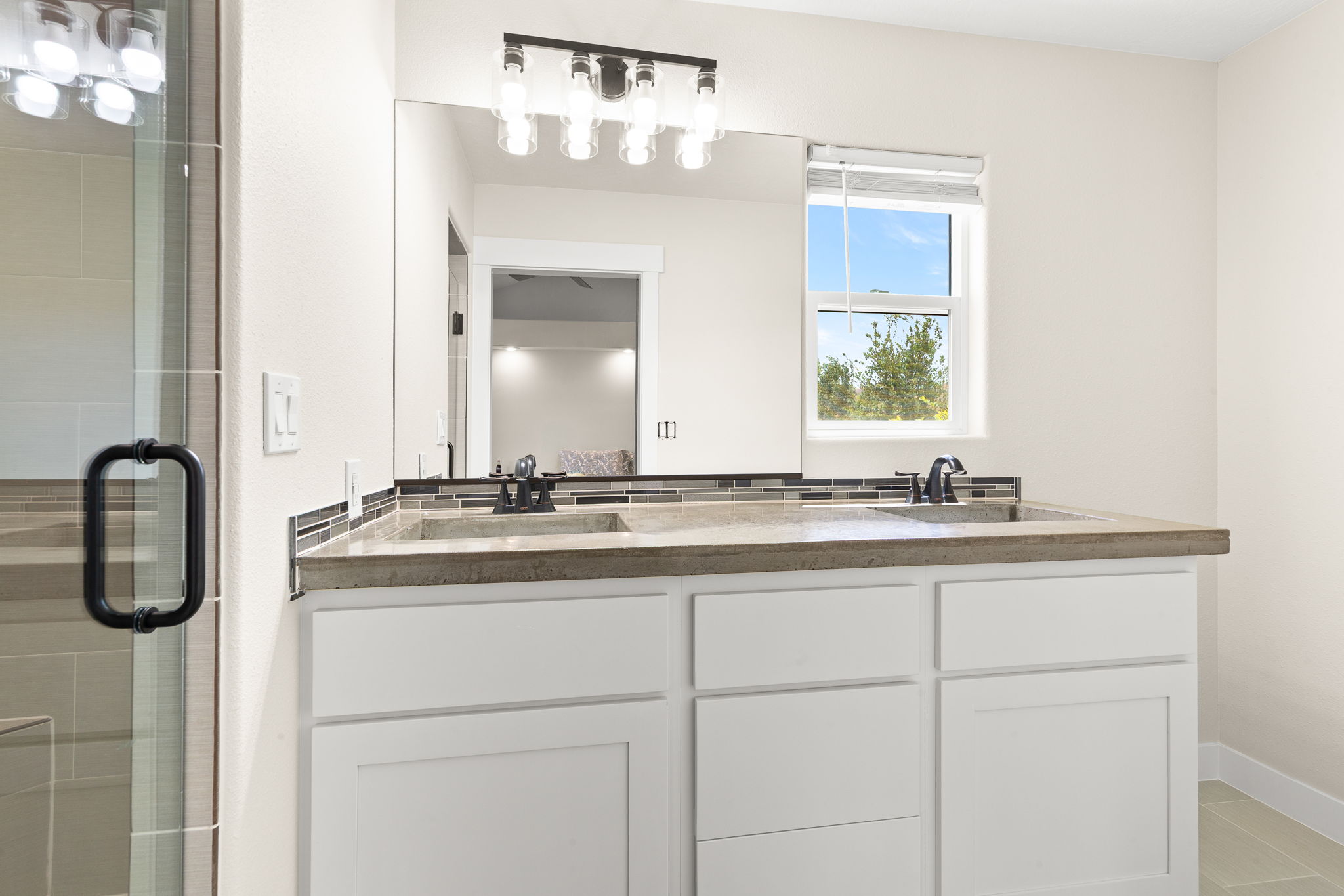 Dual-sink vanity featuring a light-toned countertop, mosaic tile backsplash, and matte black fixtures