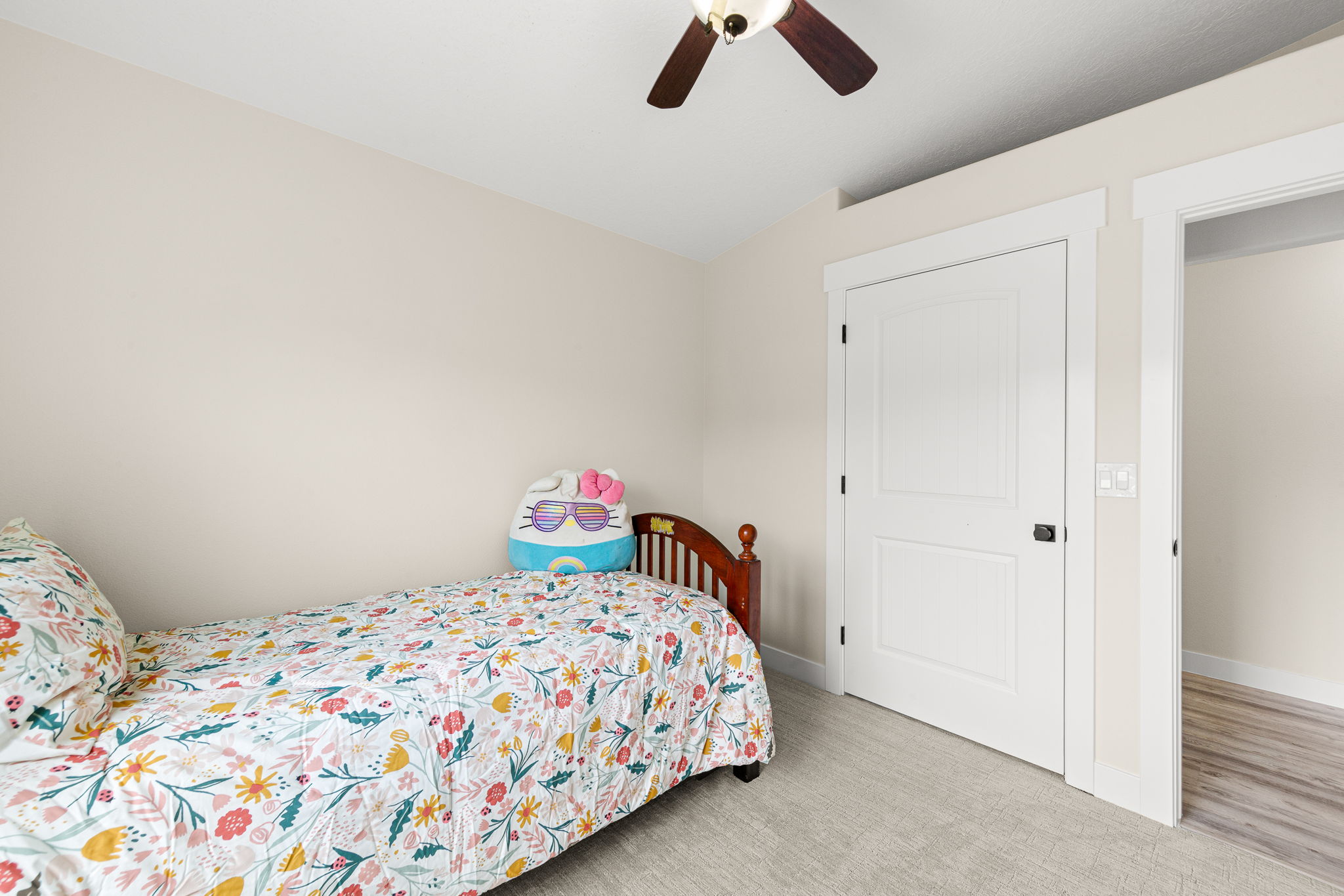 Carpeted room featuring a white two-panel door with black hardware, a ceiling fan with wood-finish blades, and neutral wall paint