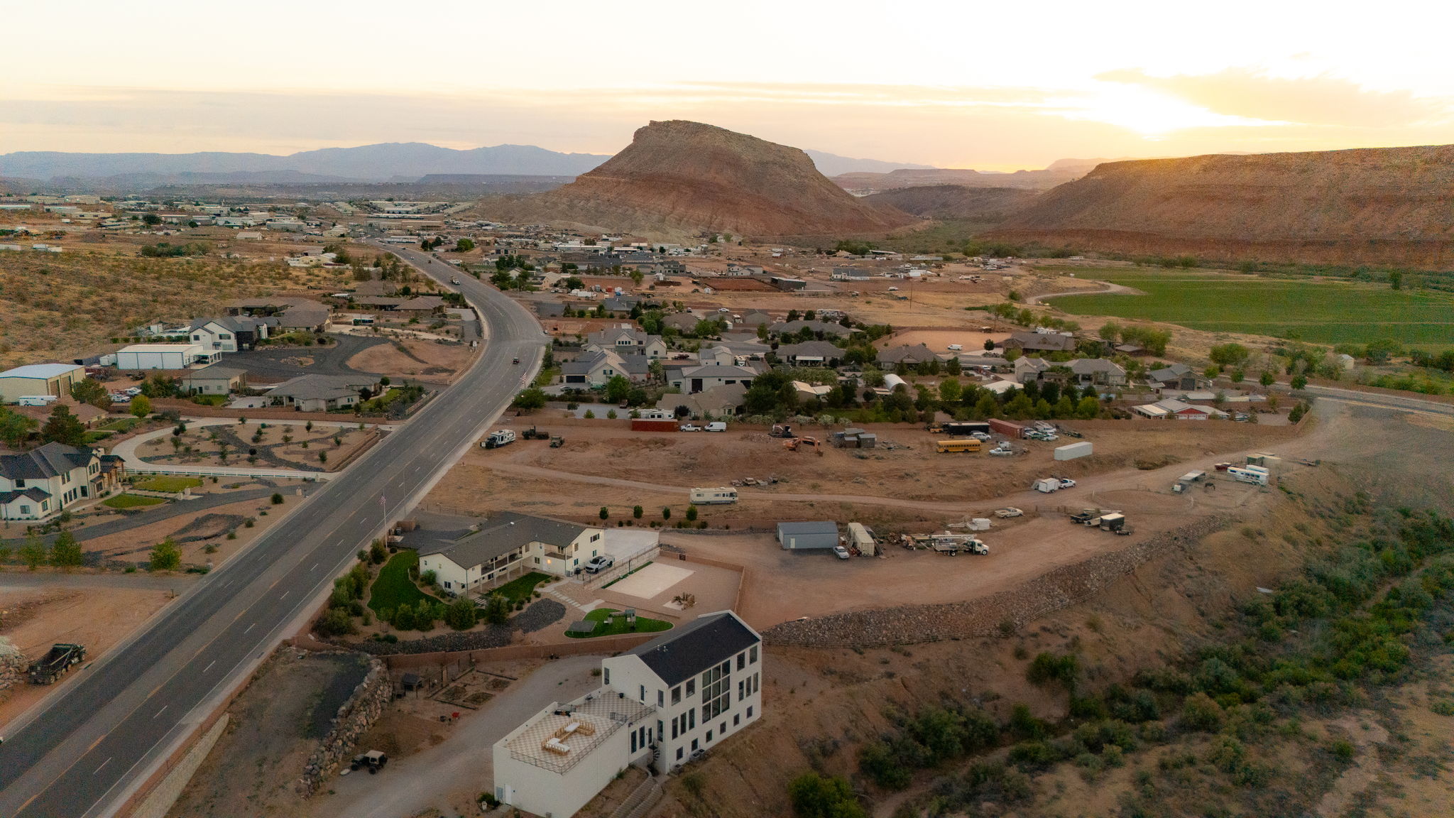 Expansive high desert landscape featuring a residential community, a winding paved road, and distant mountain formations