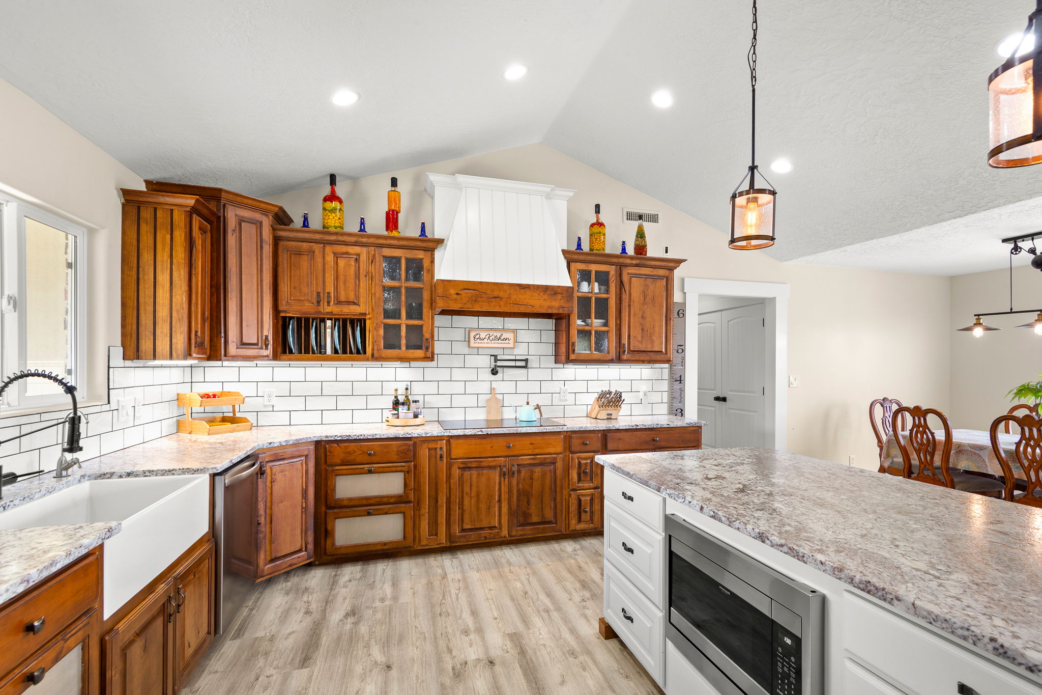 Kitchen featuring wood cabinetry, white subway tile backsplash, light-toned countertops, a farm sink, and an integrated microwave in the island