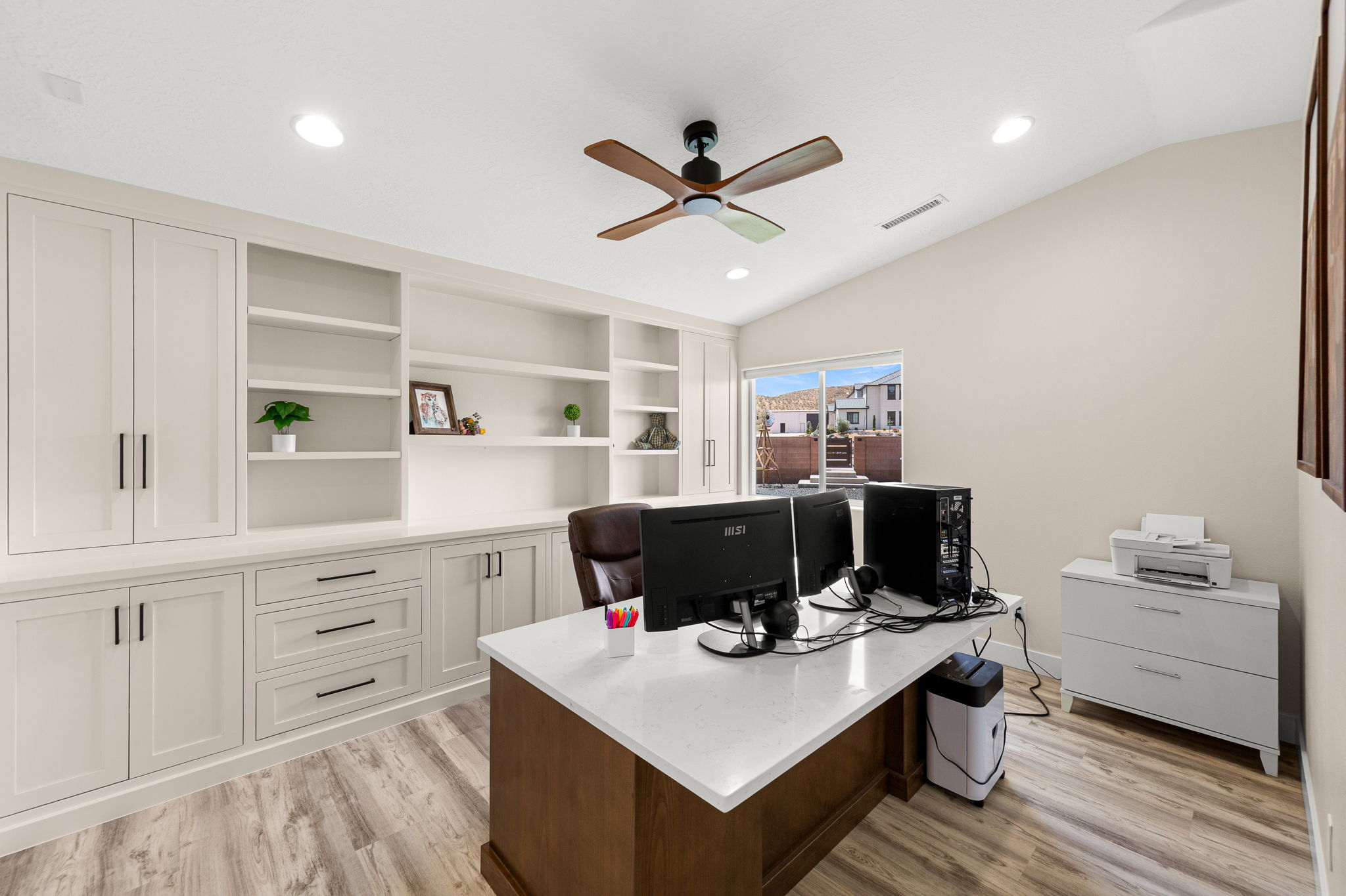 Dedicated office space featuring extensive built-in cabinetry, integrated shelving, wood-finish flooring, a vaulted ceiling, and recessed lighting