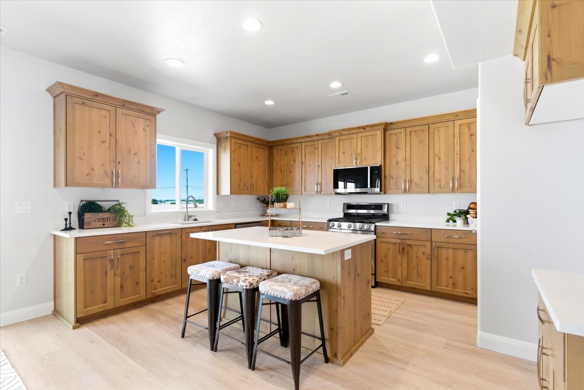 Light wood-finish cabinetry with crown molding, white countertops, stainless steel appliances, and a central island with counter seating