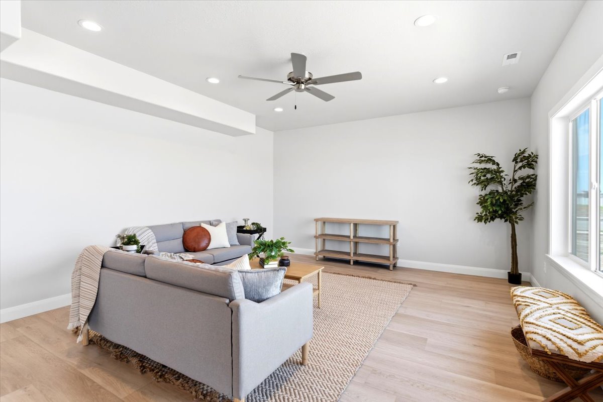 Spacious living area featuring light wood-finish flooring, recessed lighting, a ceiling fan, large windows, and a neutral color palette