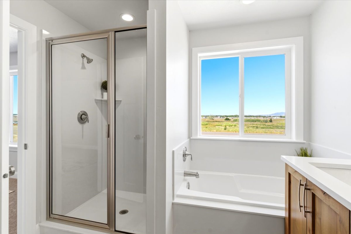 Modern bath featuring a glass-enclosed shower with a built-in shelf, a deep soaking tub, and a window presenting expansive landscape