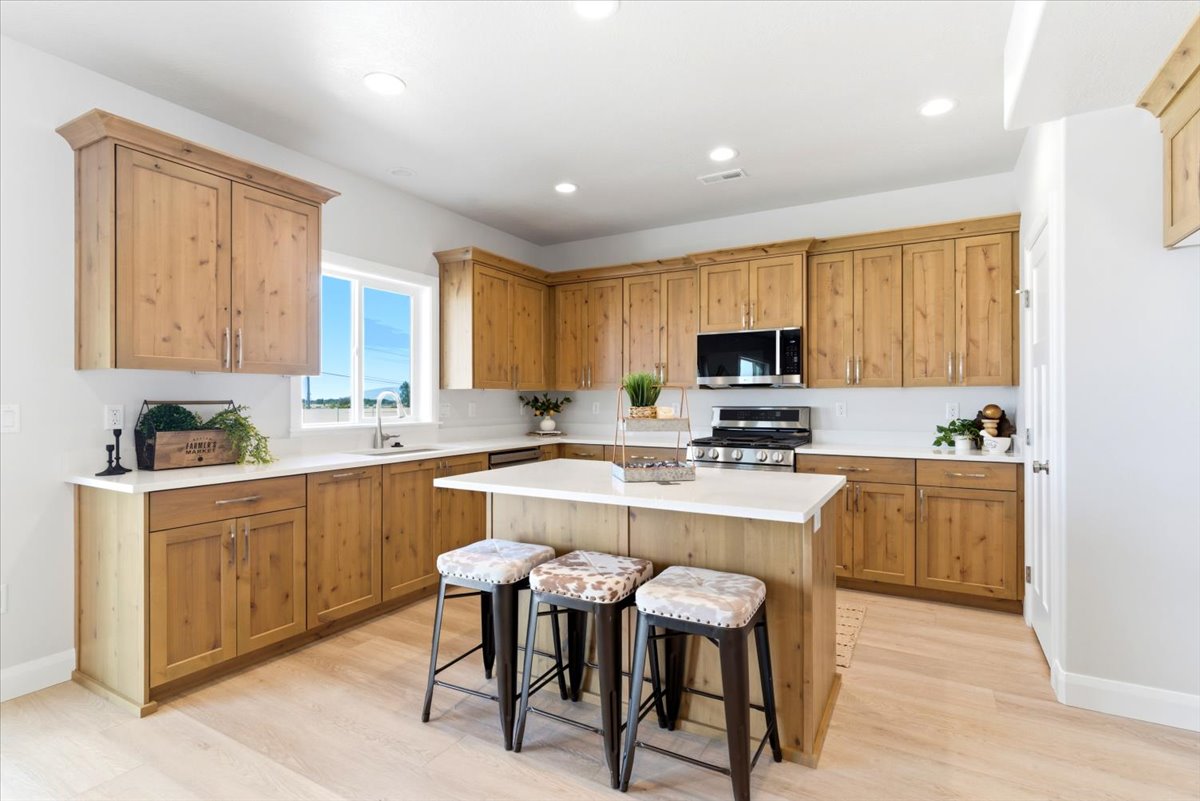 Spacious kitchen featuring light wood cabinetry, white countertops, a central island with integrated seating, stainless steel appliances, and wood-finish flooring
