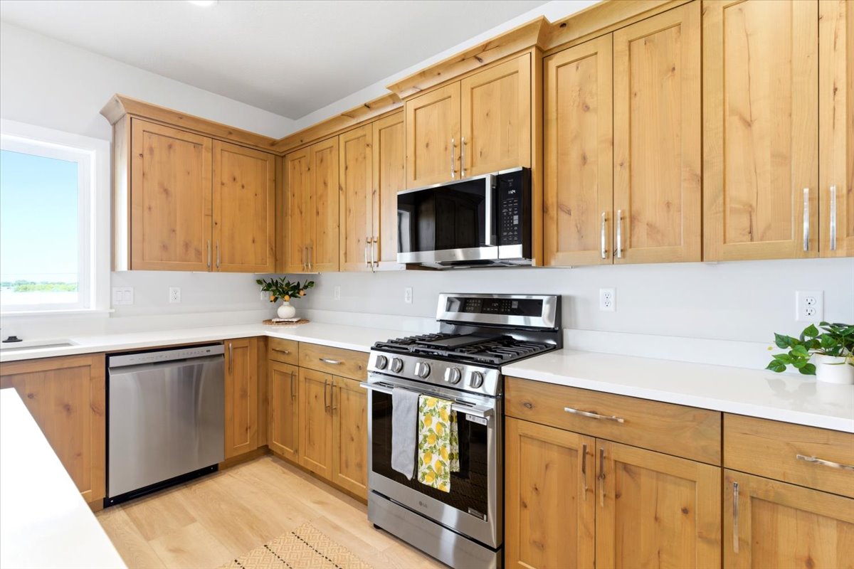 U-shaped kitchen featuring wood cabinetry with chrome hardware, white countertops, stainless steel appliances, and wood-finish flooring
