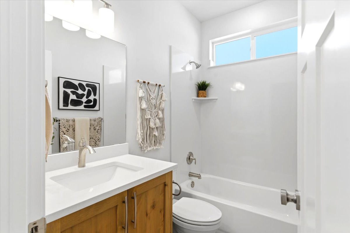 Bathroom featuring a wood-finish vanity with a white countertop and integrated sink, brushed nickel faucet, large mirror, and a full-size bathtub with a shower
