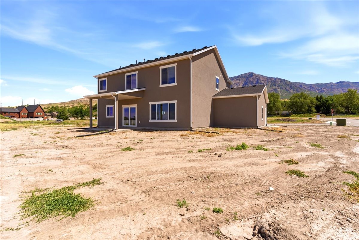 Stucco exterior with a covered patio, multiple windows, and a mountain backdrop