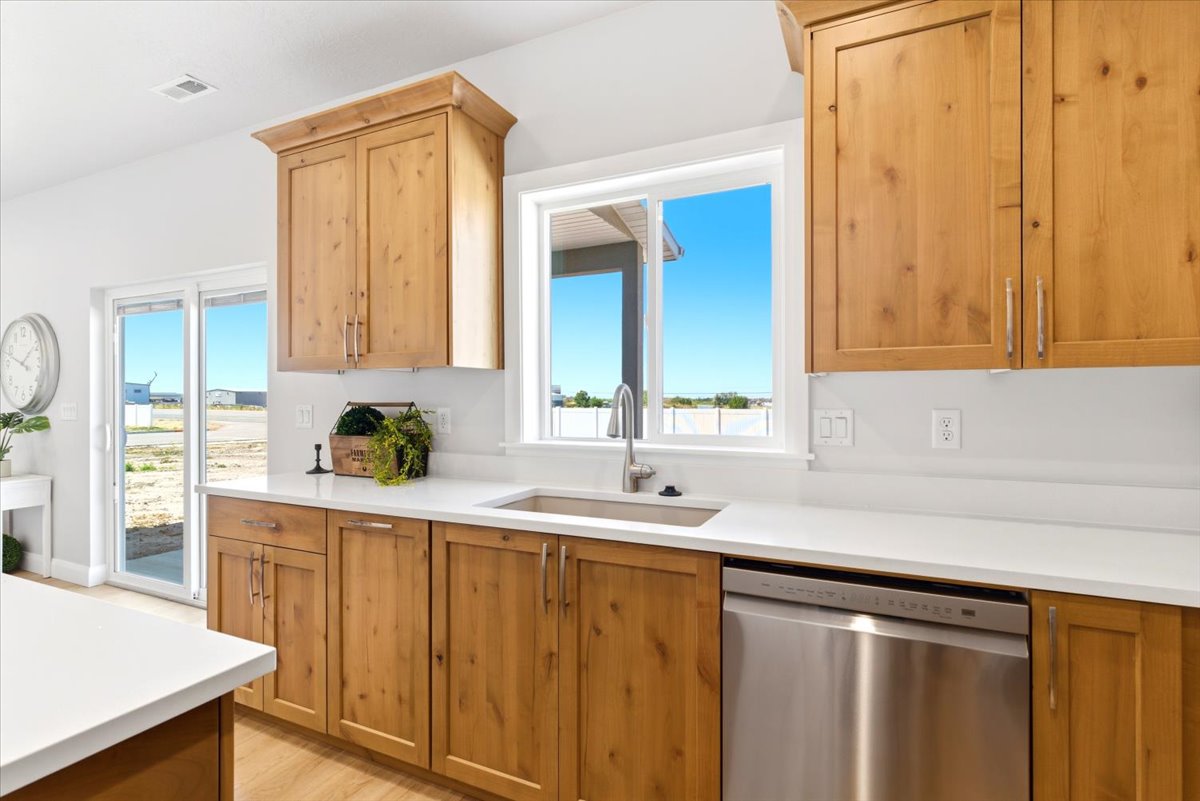Kitchen featuring light wood-finish cabinetry, white countertops, a stainless steel sink with a gooseneck faucet, a stainless steel dishwasher, and a window above the sink