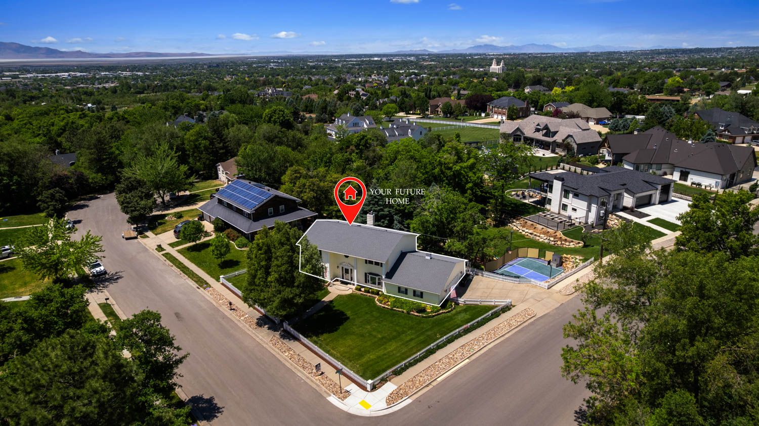 Corner lot residence featuring a light-colored exterior, green lawn, mature trees, and a paved driveway
