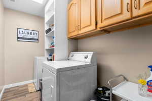 Dedicated laundry area featuring wood-finish flooring, ample built-in cabinetry, and integrated shelving for storage