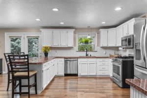 Kitchen featuring white cabinetry, brown granite-style countertops, stainless steel appliances, wood-finish flooring, and recessed lighting