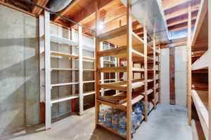 Dedicated storage room featuring multiple built-in wooden shelving units, concrete walls, exposed ceiling joists, and a concrete floor