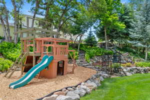 Expansive backyard featuring a wood-built playset on wood chip ground cover, a manicured lawn, stone retaining walls, and a decorative metal archway