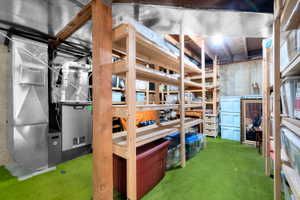 Utility room featuring a furnace unit, exposed ductwork, concrete walls, and green low-pile carpeting
