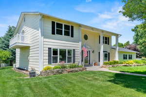 Classic two-story residence featuring a covered front entry with columns, a second-story balcony with white railing, and dark louvered shutters