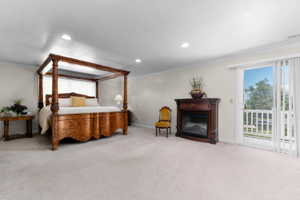 Spacious room featuring light-colored carpeting, a built-in fireplace with a dark wood mantel, recessed lighting, and a sliding glass door leading to an outdoor balcony with white railings