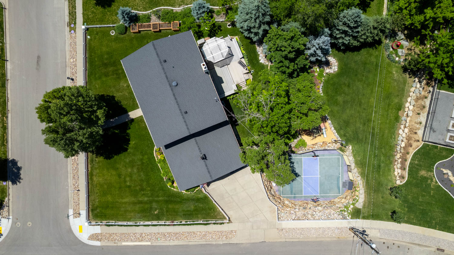 Expansive property featuring a multi-sport court, substantial green spaces, mature trees, and a tiered rock landscaping