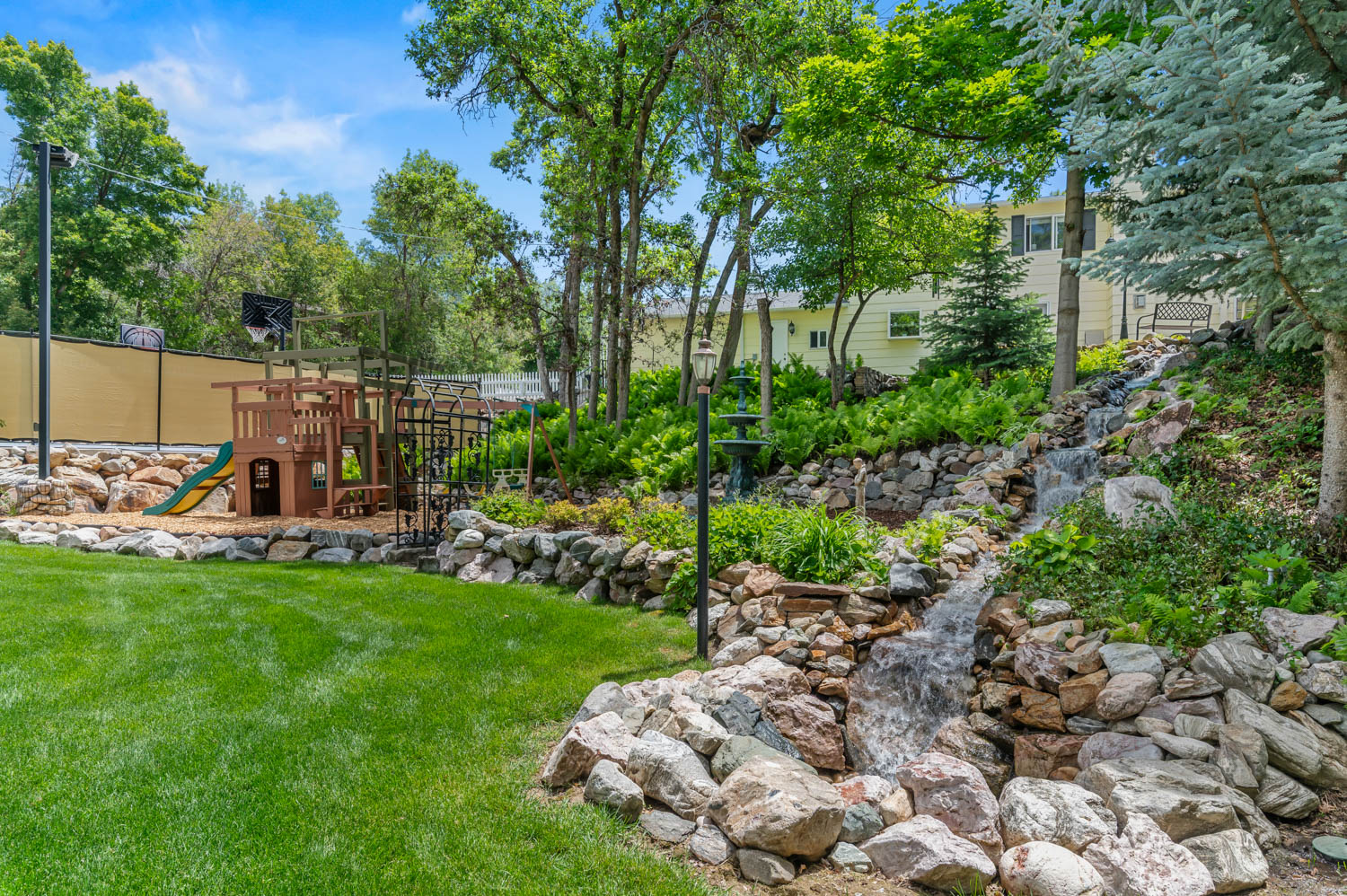 Expansive backyard featuring a multi-tiered rock waterfall, lush green lawn, and mature trees