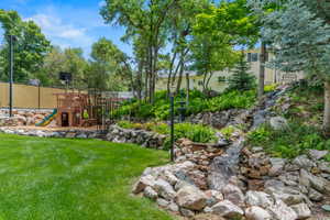 Expansive backyard featuring a multi-tiered rock waterfall, lush green lawn, and mature trees