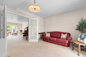 White French doors opening into a carpeted interior space with a chandelier light fixture
