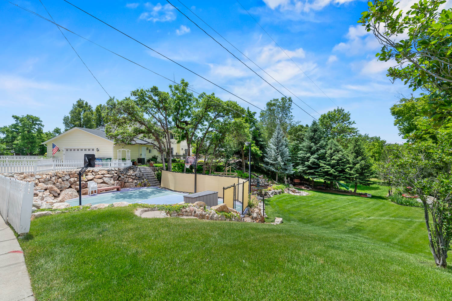 Expansive outdoor space featuring a half-court sports court, a stone retaining wall, and a verdant lawn area