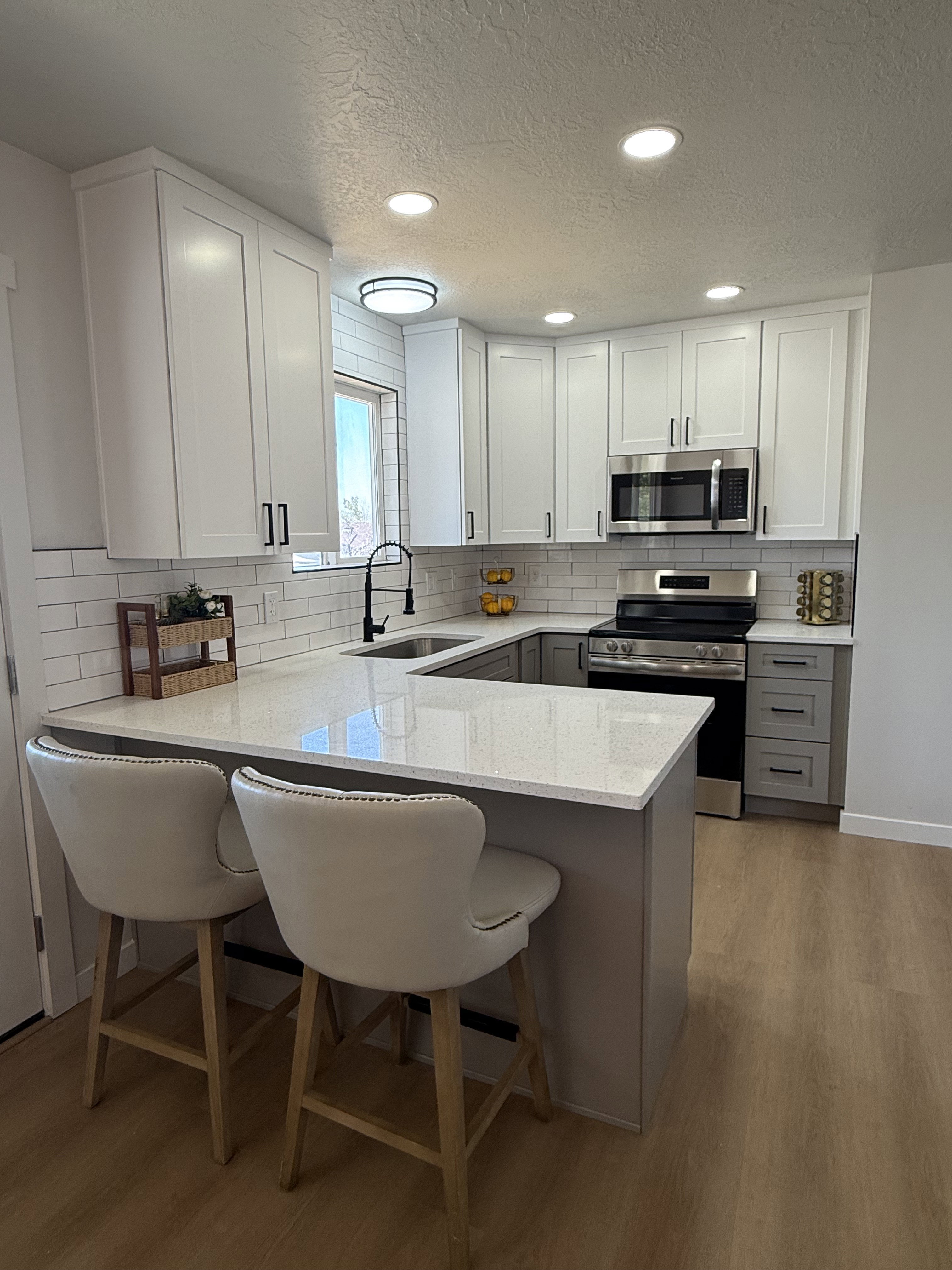 Modern kitchen with light wood-finish flooring, white upper cabinetry, and gray base cabinetry