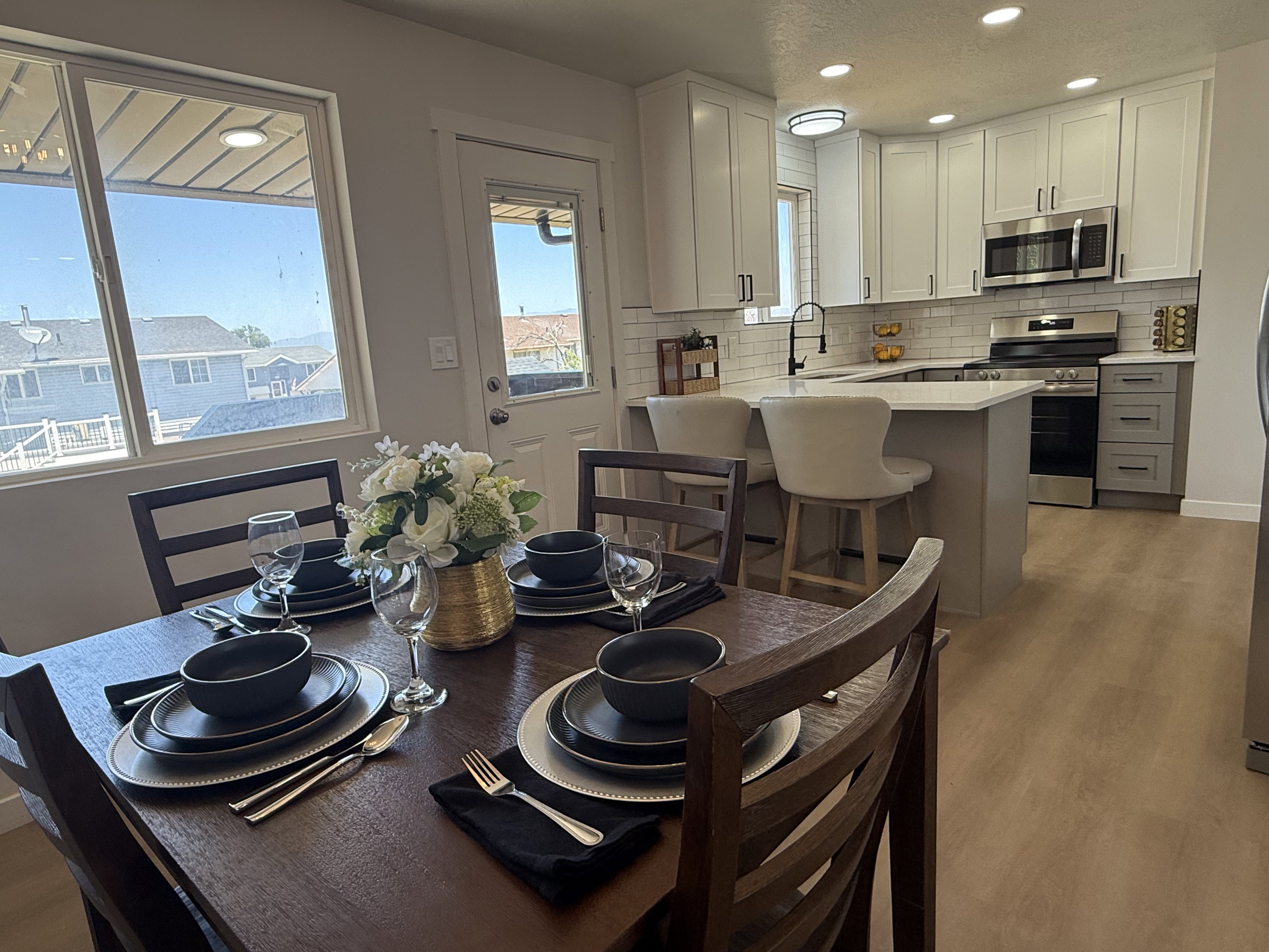 Open-concept kitchen and dining area featuring light-finish flooring, white shaker cabinetry, stainless steel appliances, a white subway tile backsplash, and a breakfast bar with seating