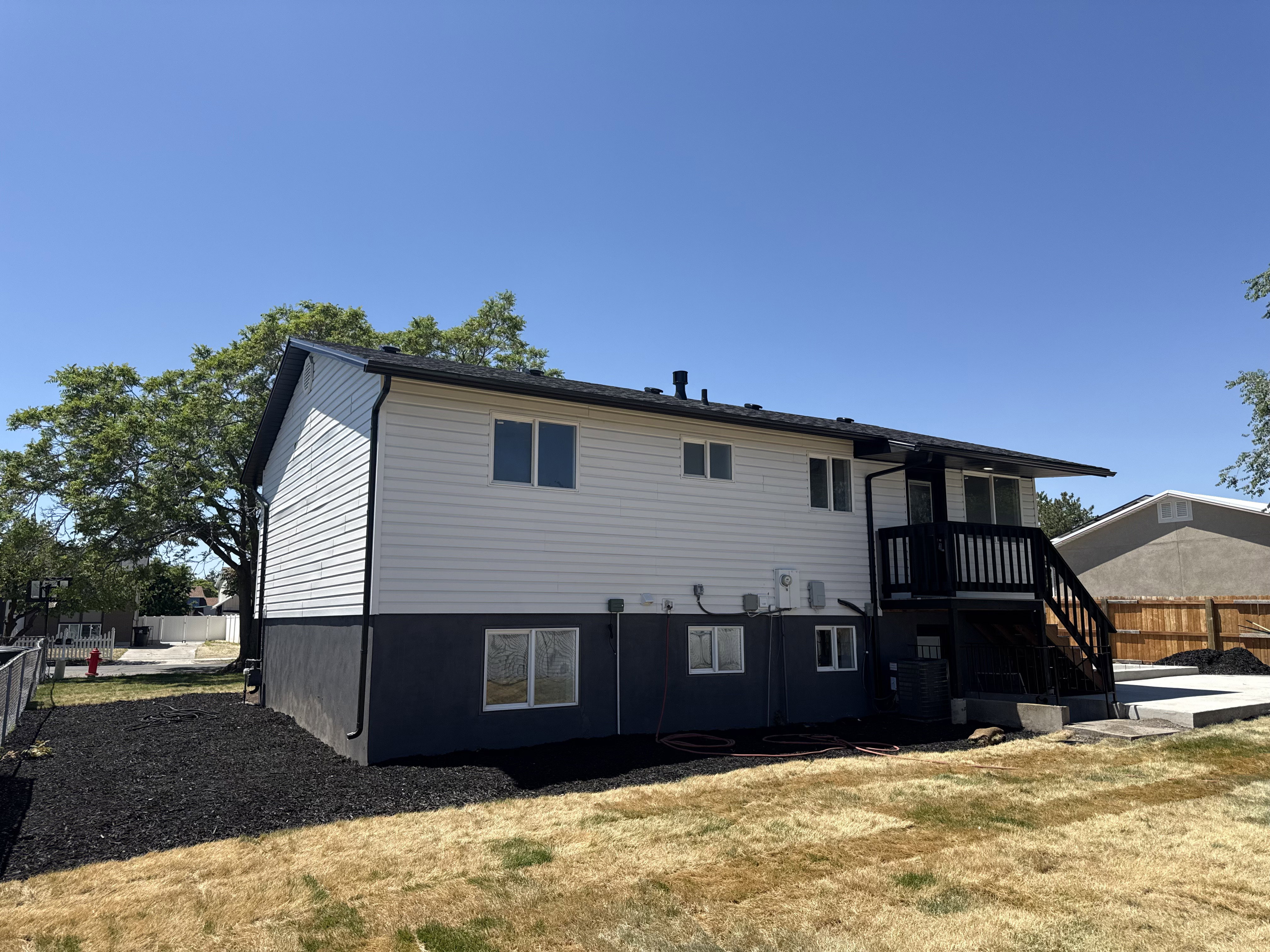 Rear exterior featuring white horizontal siding, a black painted foundation, and a black deck with stairs