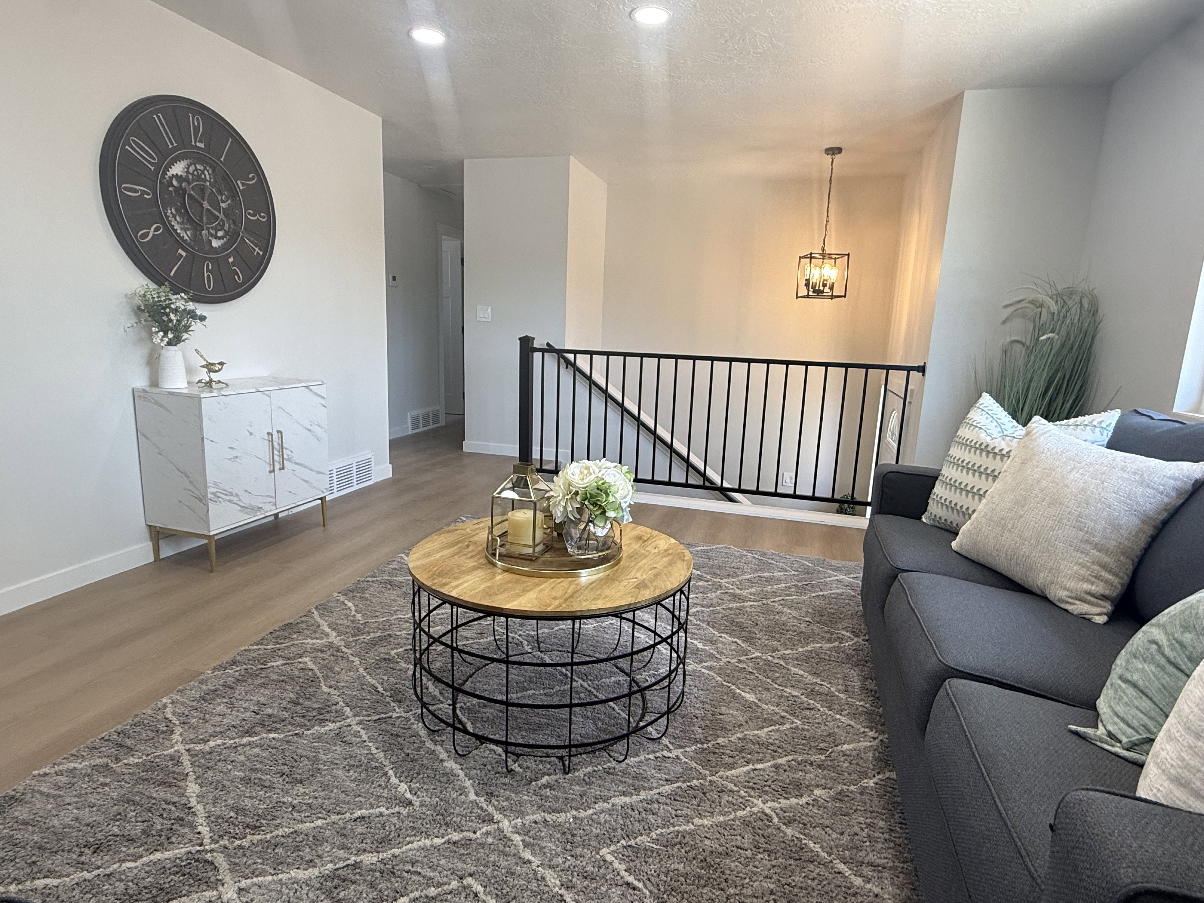 Open-concept living area featuring wood-finish flooring, recessed lighting, and a black metal staircase railing