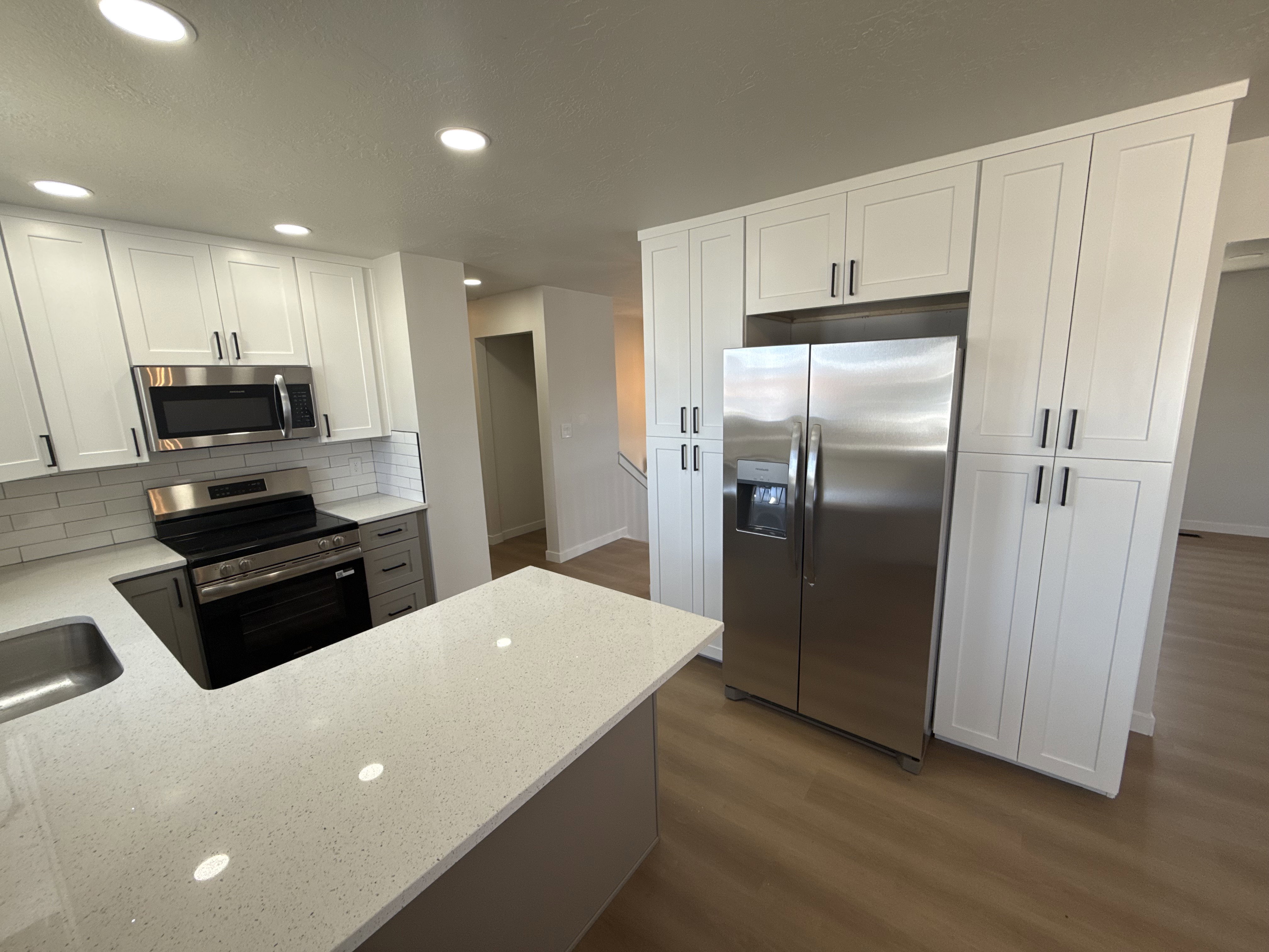 Open-concept kitchen featuring white shaker cabinetry, stainless steel appliances, and a built-in refrigerator