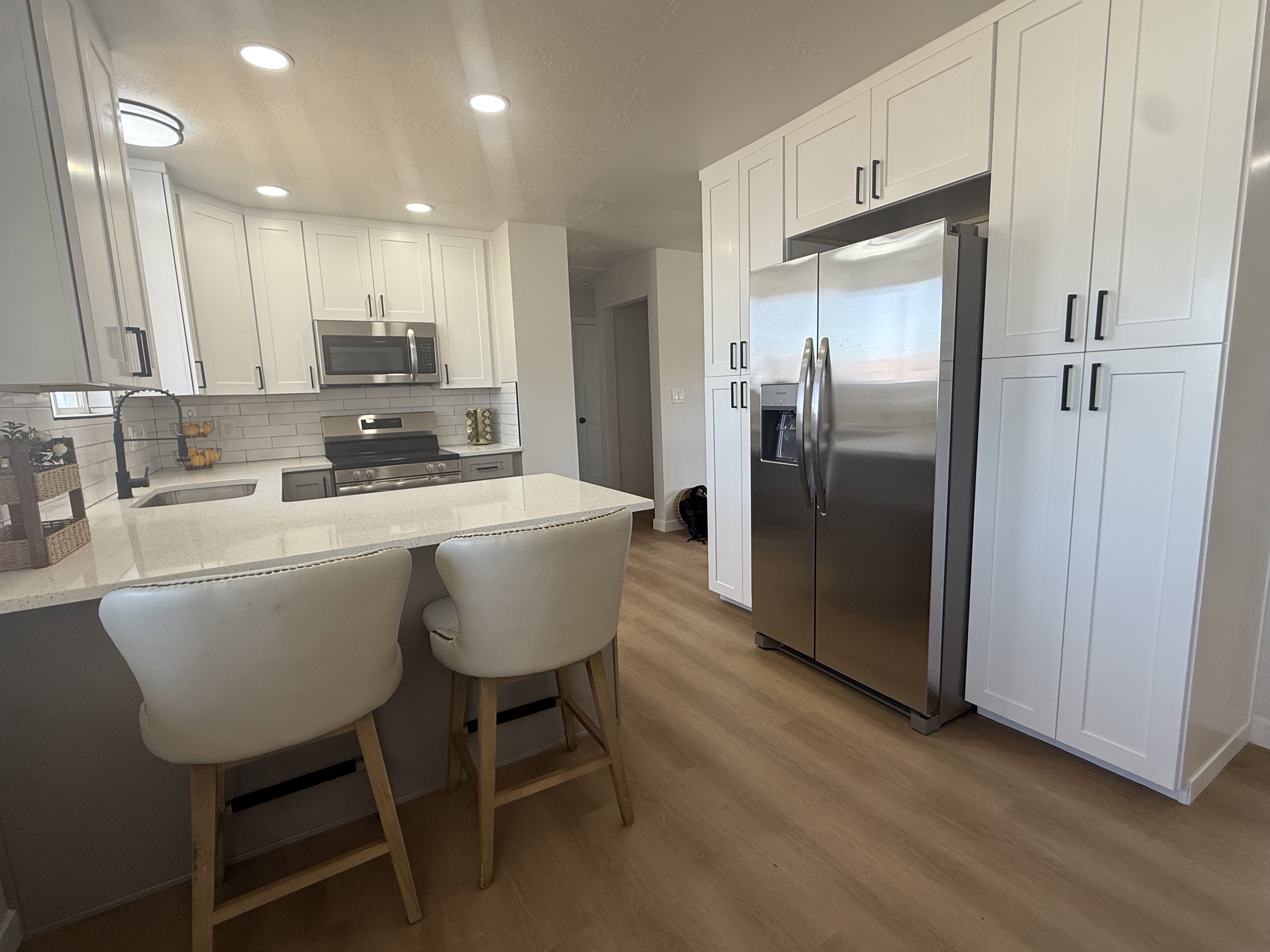 Modern kitchen featuring white shaker-style cabinetry, stainless steel appliances, light-toned countertops, subway tile backsplash, and wood-finish flooring