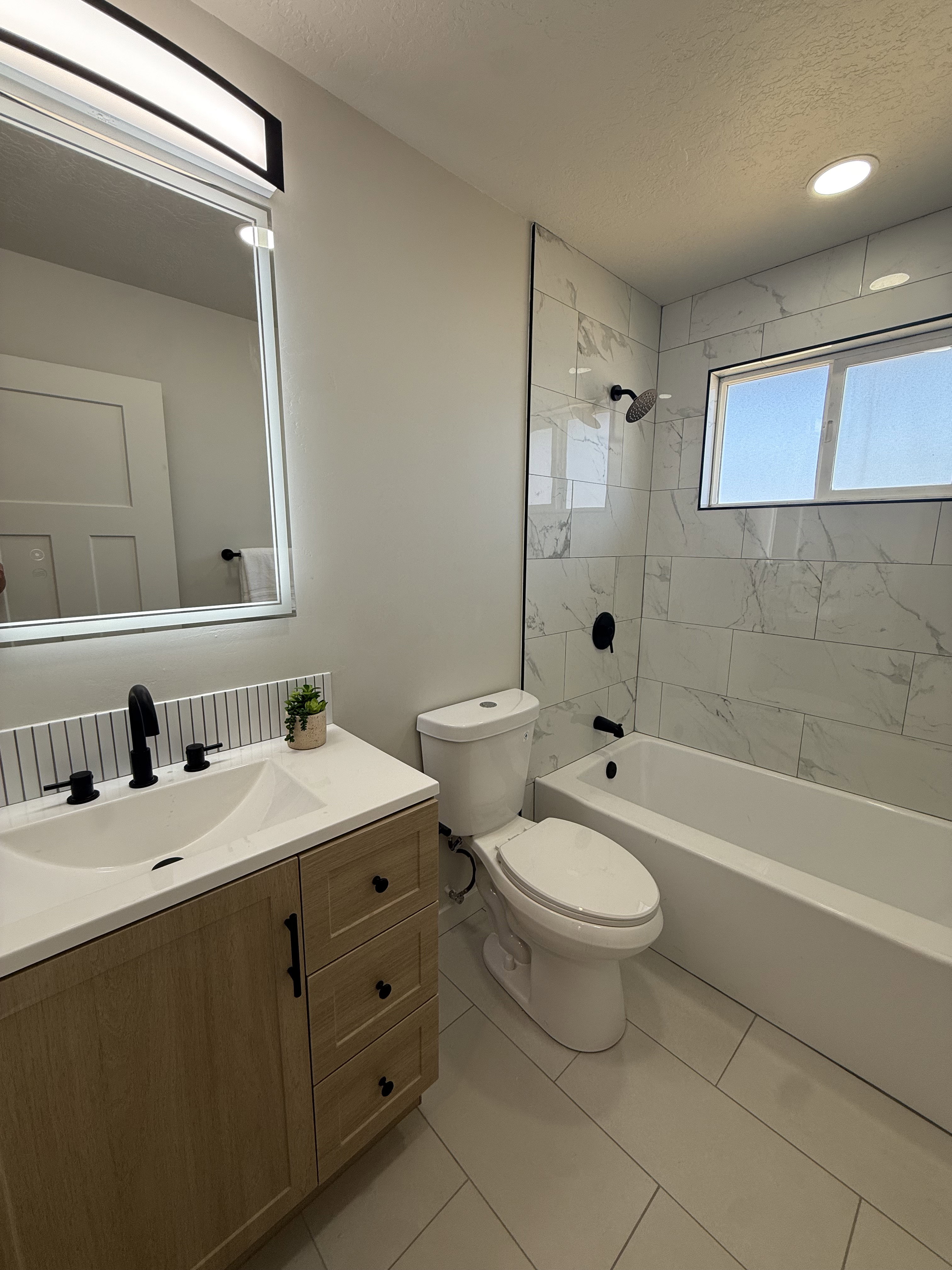Bathroom featuring a light wood-finish vanity with a white countertop and integrated sink, matte black fixtures, and a subway tile backsplash