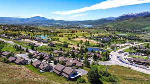 Expansive aerial view showcasing residential properties, a golf course with water features, distant lakes, and snow-capped mountains under a clear sky