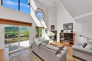 Vaulted living room featuring wood-finish flooring, a stone-surround fireplace, and a large sliding glass door opening to an outdoor deck