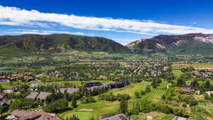 Expansive aerial overview showcasing a golf course, numerous residential structures, substantial green spaces, and surrounding mountainous terrain