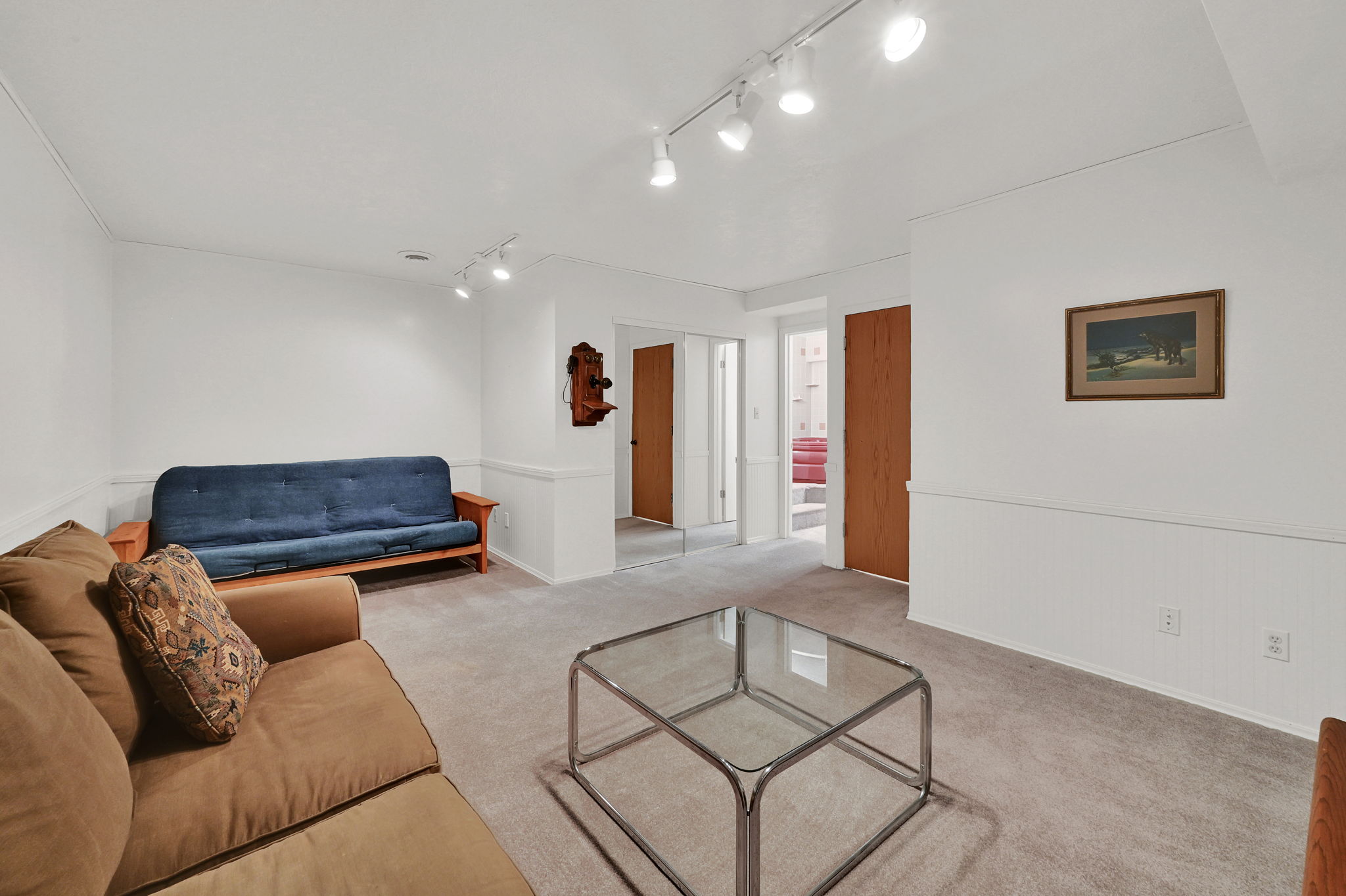 Carpeted room featuring white walls with wainscoting, track lighting, and wood-finish doors