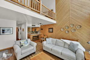 Living area featuring wood-finish flooring, a wood-paneled accent wall, a built-in kitchen island with seating, an open-concept layout, and a lofted space with a log railing