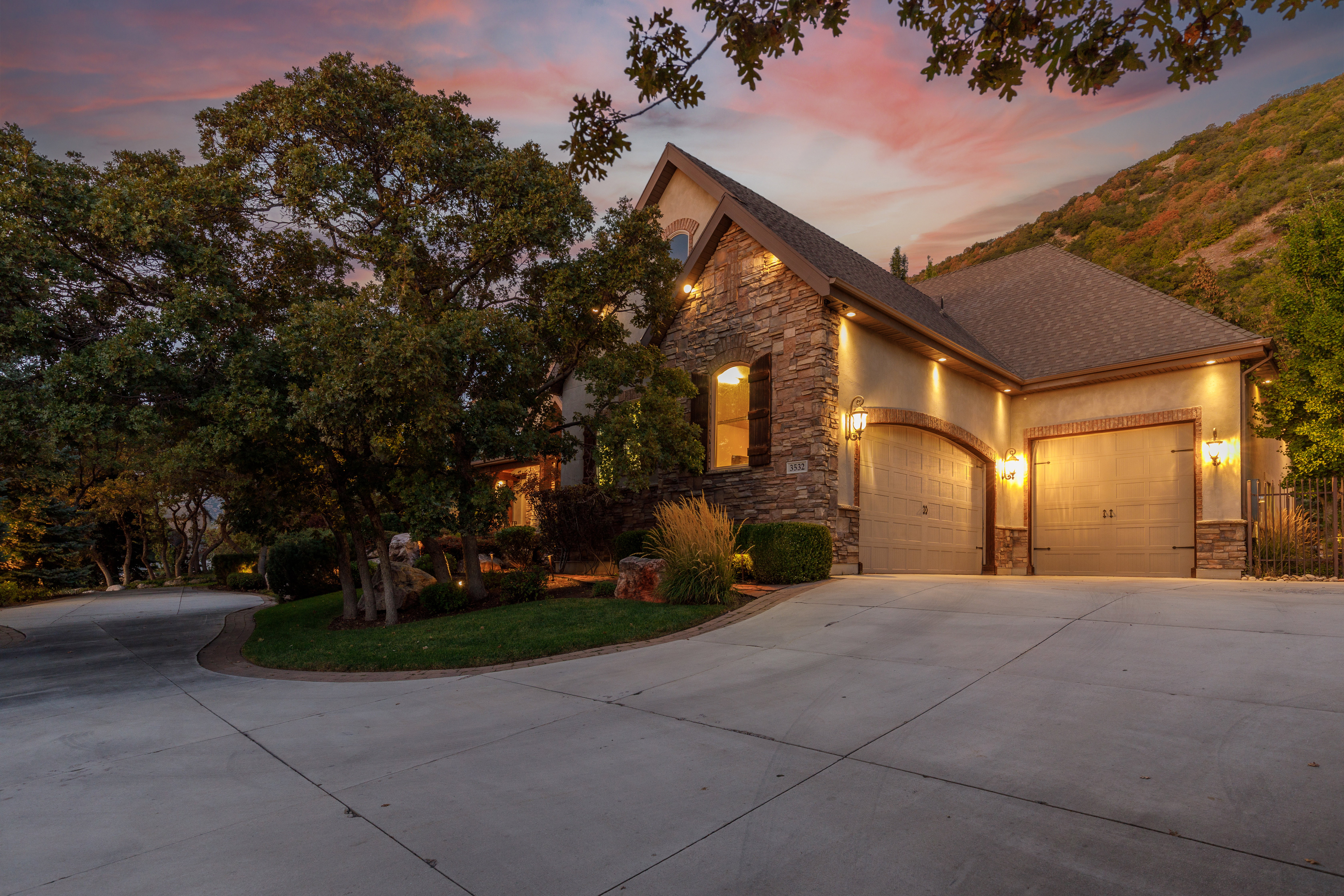 Stucco and stone facade home featuring a two-car garage with arched entrances and exterior sconce lighting