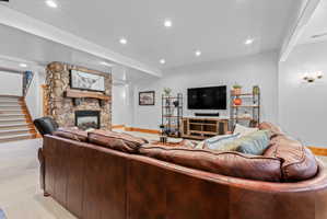 Spacious living area featuring a floor-to-ceiling stone fireplace with a wood mantel, recessed lighting, wall sconces, and a carpeted staircase