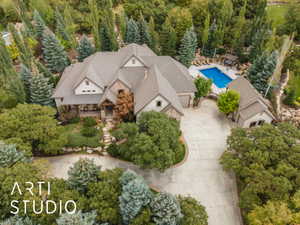Expansive estate featuring a multi-gabled roofline, stone and stucco exterior, covered front porch, an in-ground swimming pool, and a detached auxiliary structure