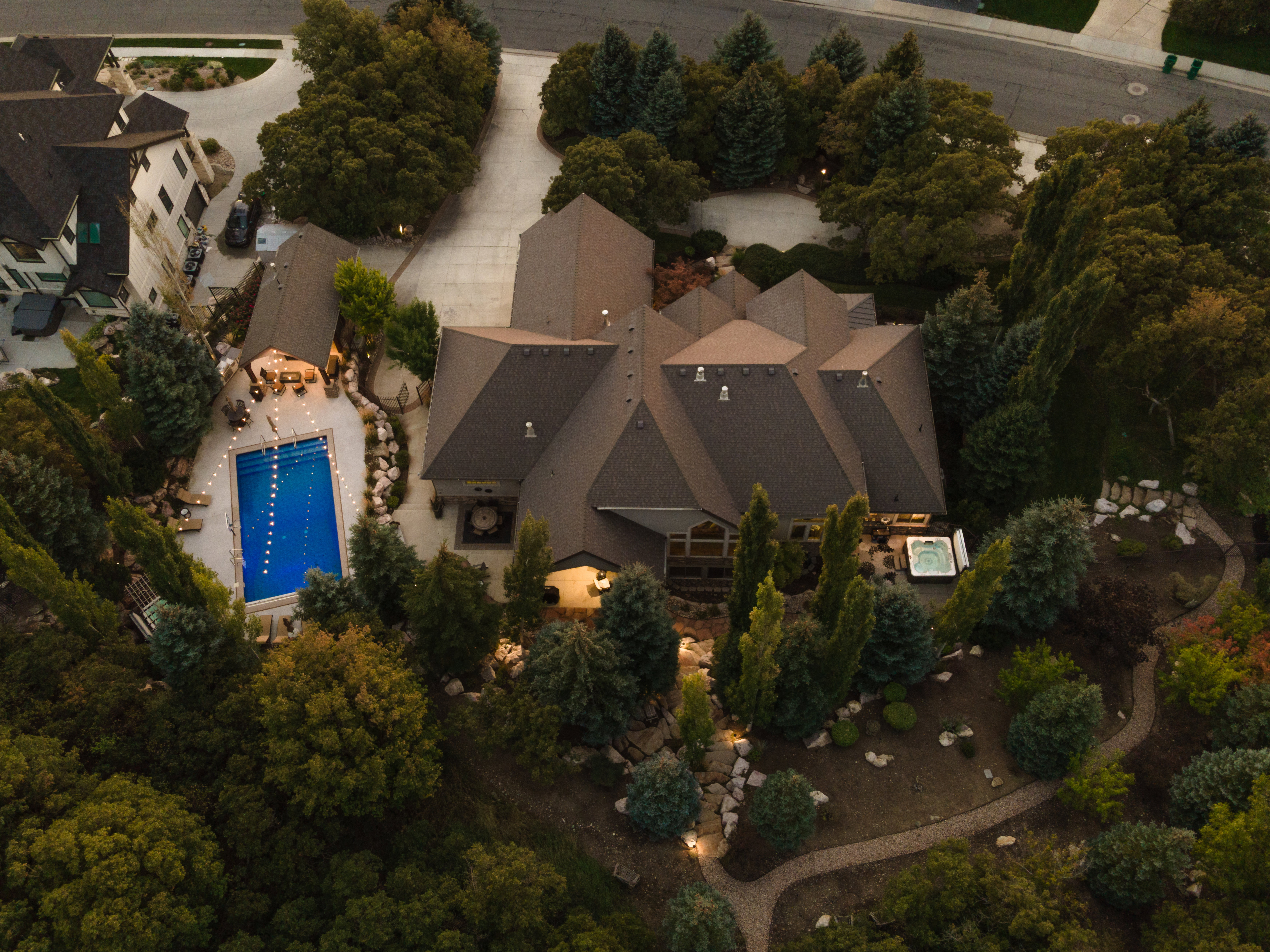 Expansive property featuring a multi-gabled main residence, an in-ground swimming pool with surrounding patio, a separate outdoor spa, mature landscaping, and an extensive paved driveway