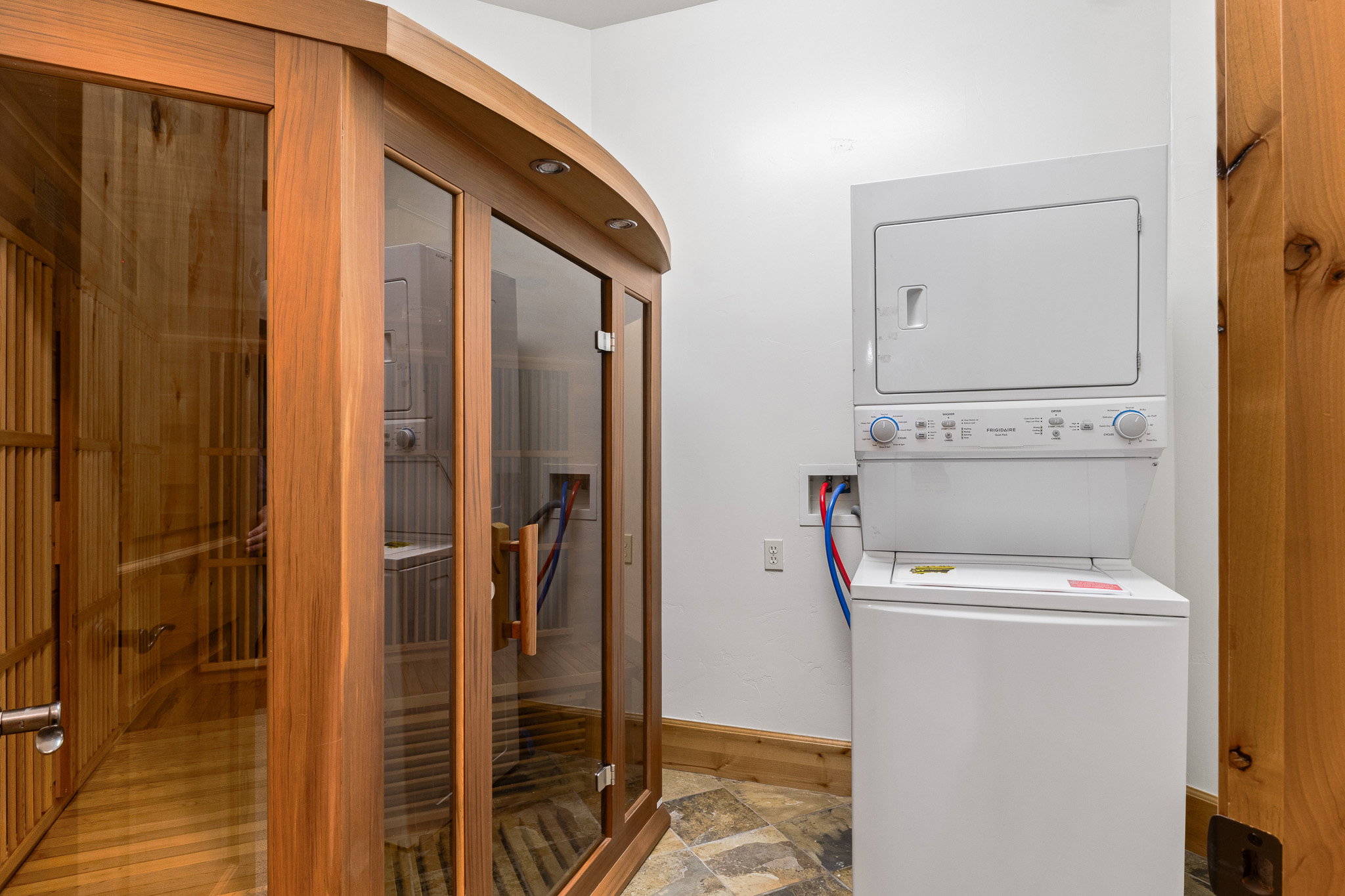 Wood-framed sauna with glass doors and wood-finish interior, complemented by a stacked washer and dryer unit