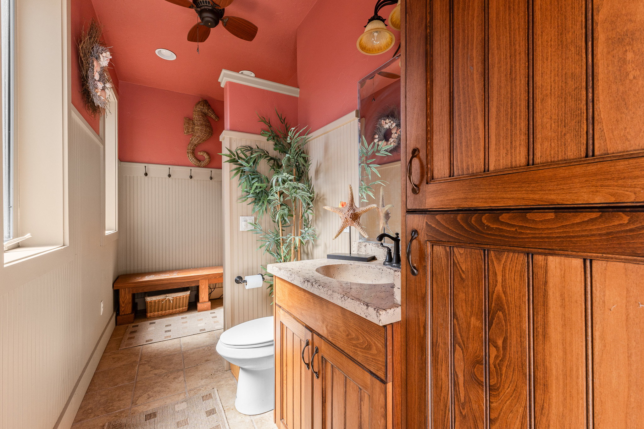 Powder room featuring wood-finish cabinetry, a stone countertop with an integrated basin, beadboard wainscoting, and tile flooring